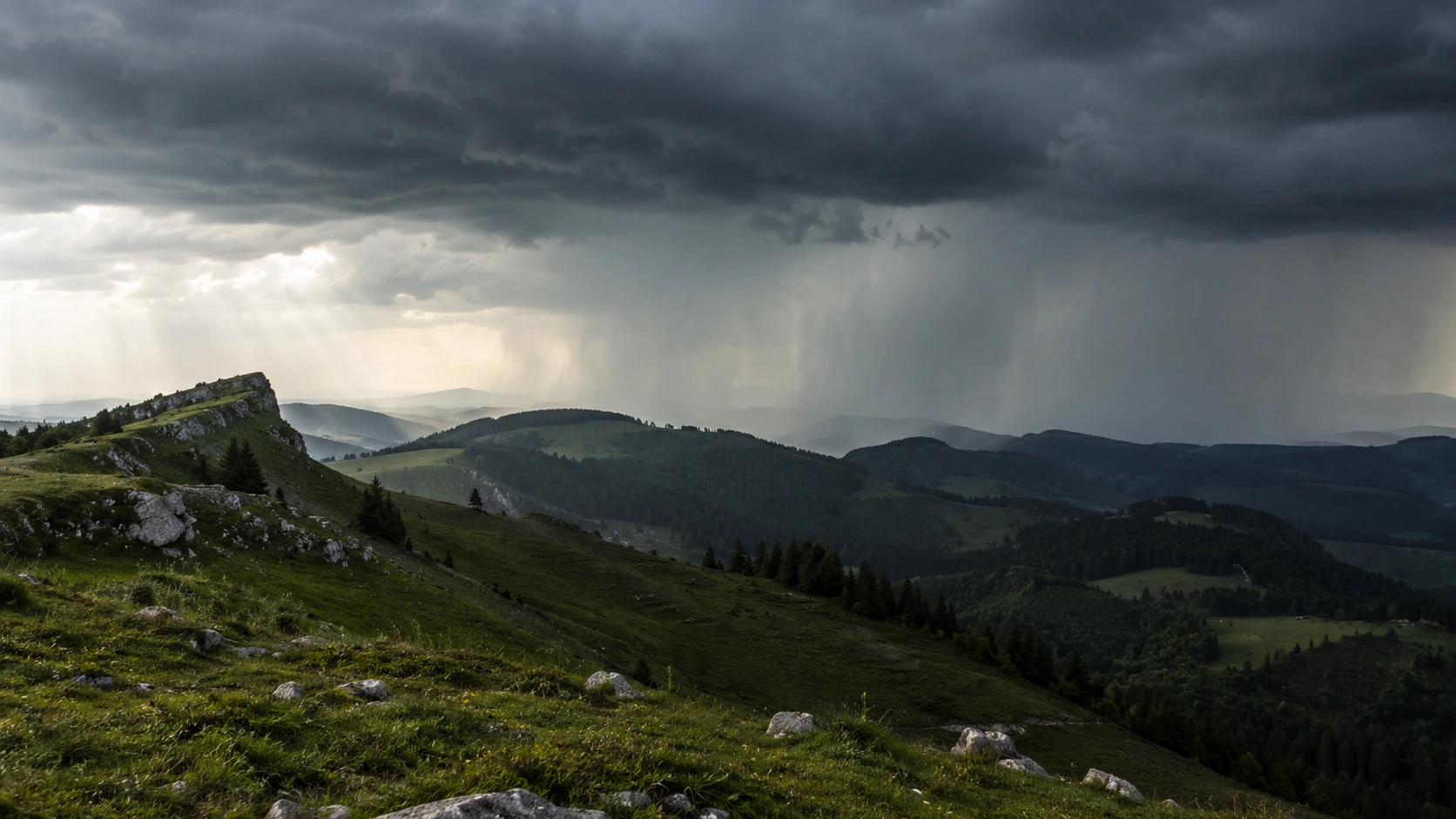 Grüne Jura- oder Voralpenlandschaft unter dunklen Wolken und entfernten Regenschauern.