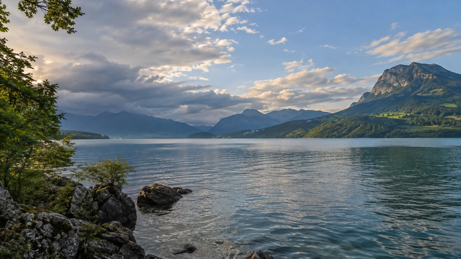 Ruhiger Schweizer See mit Bergen und zunehmender Bewölkung am Horizont.
