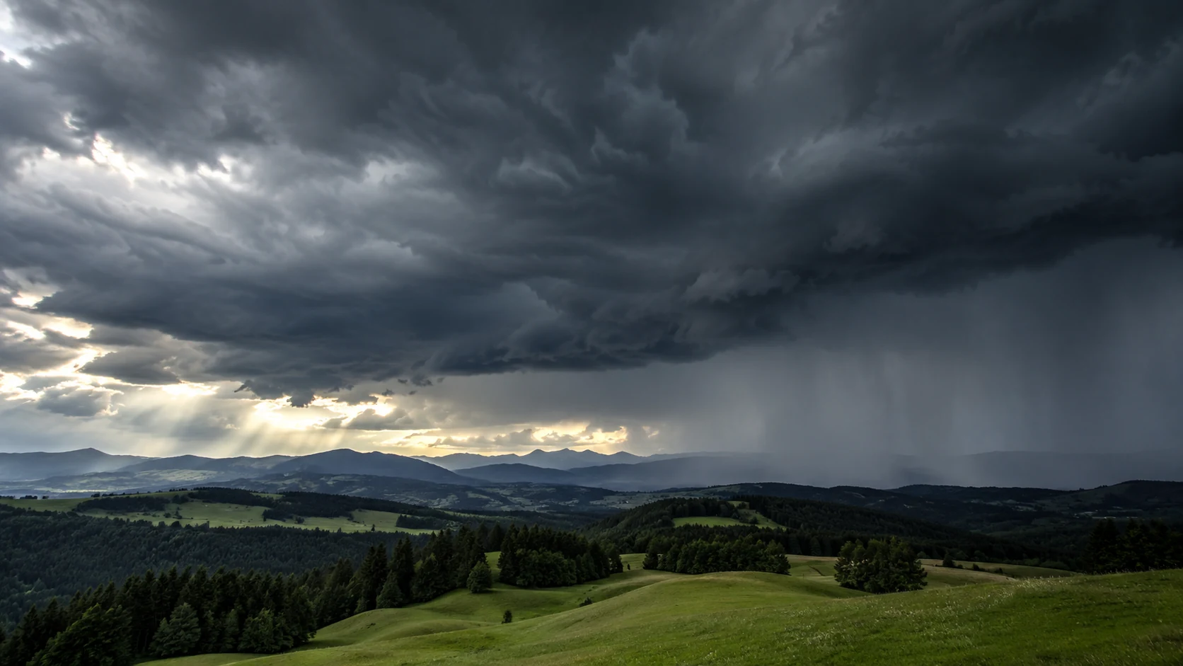 Dunkle Gewitterwolken über grünen Berglandschaften in der Schweiz vor einem Wetterumschwung.