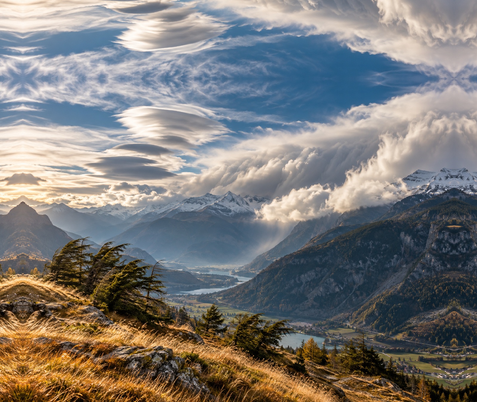 Dynamische Föhnwolken und stark vom Wind gebogene Bäume über einem Schweizer Alpental als Symbolbild für kräftigen Föhn.
